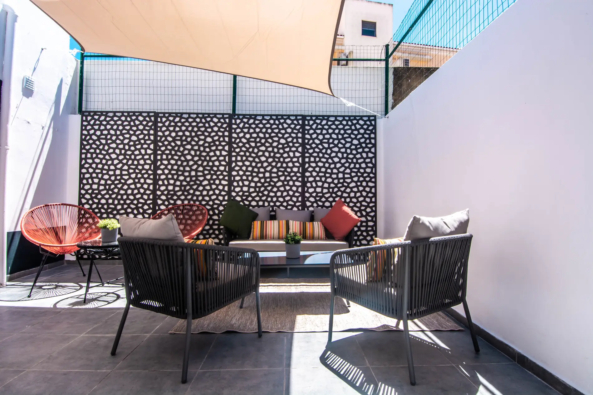 Modern outdoor patio with chairs, sofa, cushions, and a patterned privacy screen.