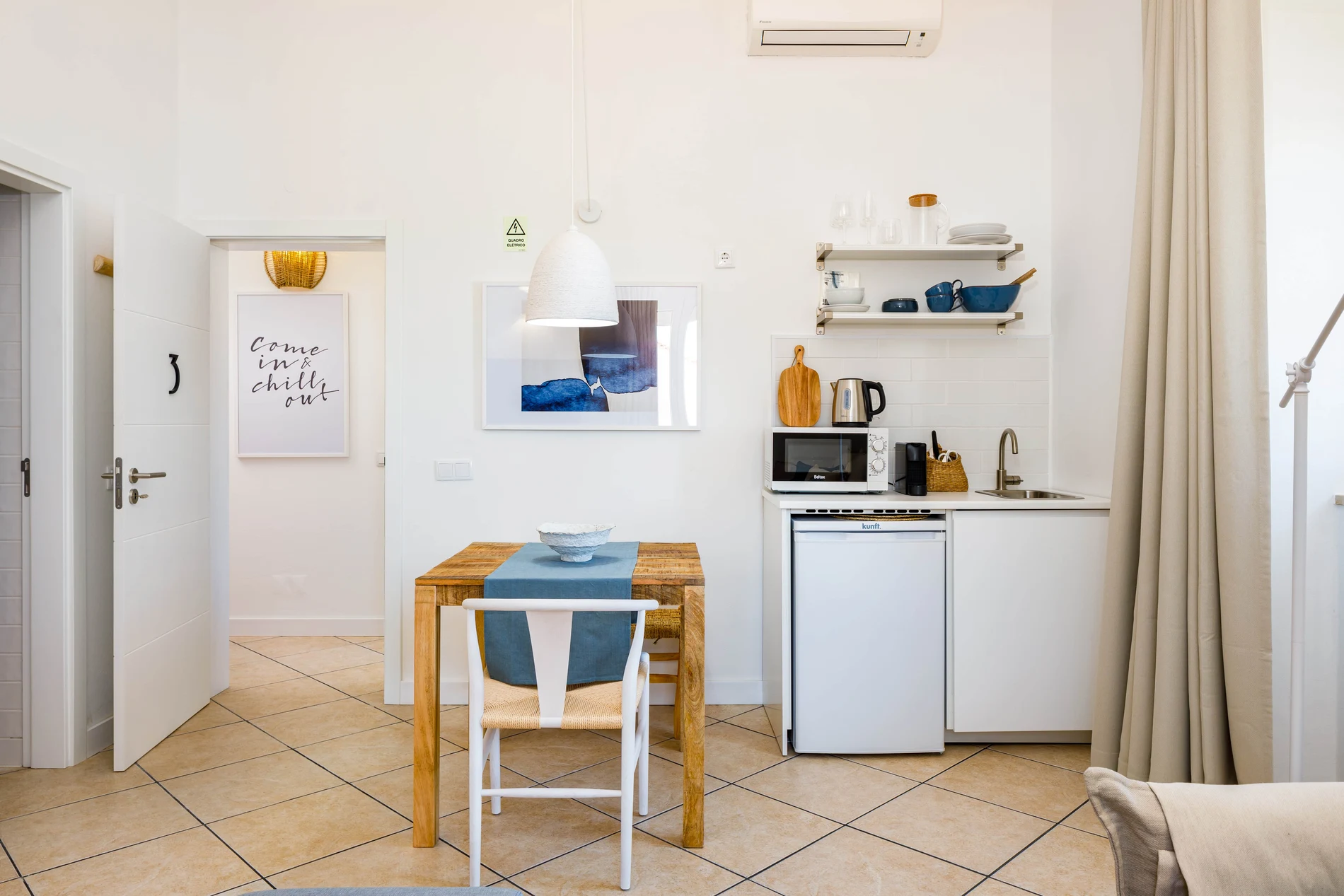 Cozy kitchenette with wooden table, white appliances, and a modern wall quote.