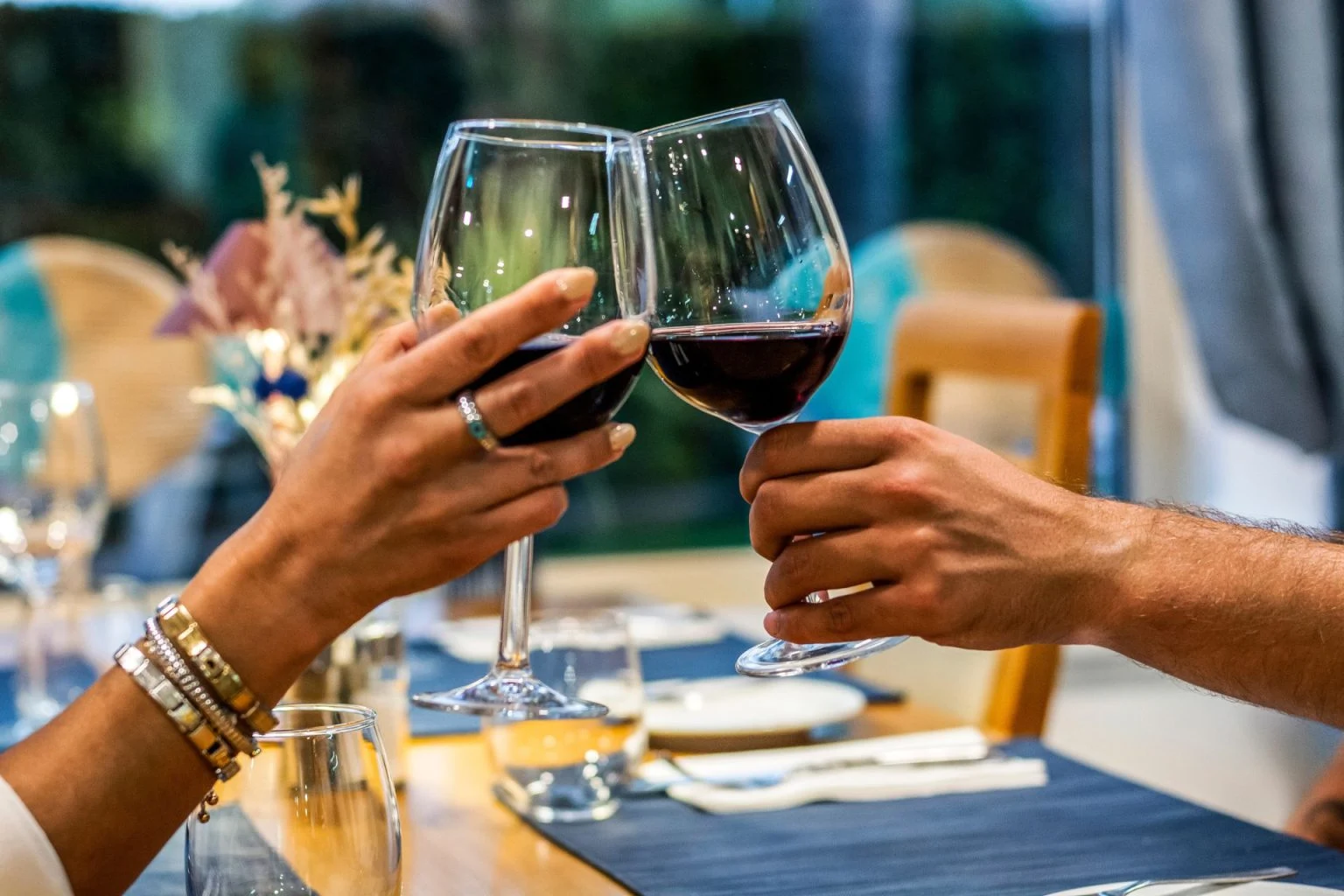 Two hands clinking wine glasses over a dining table.