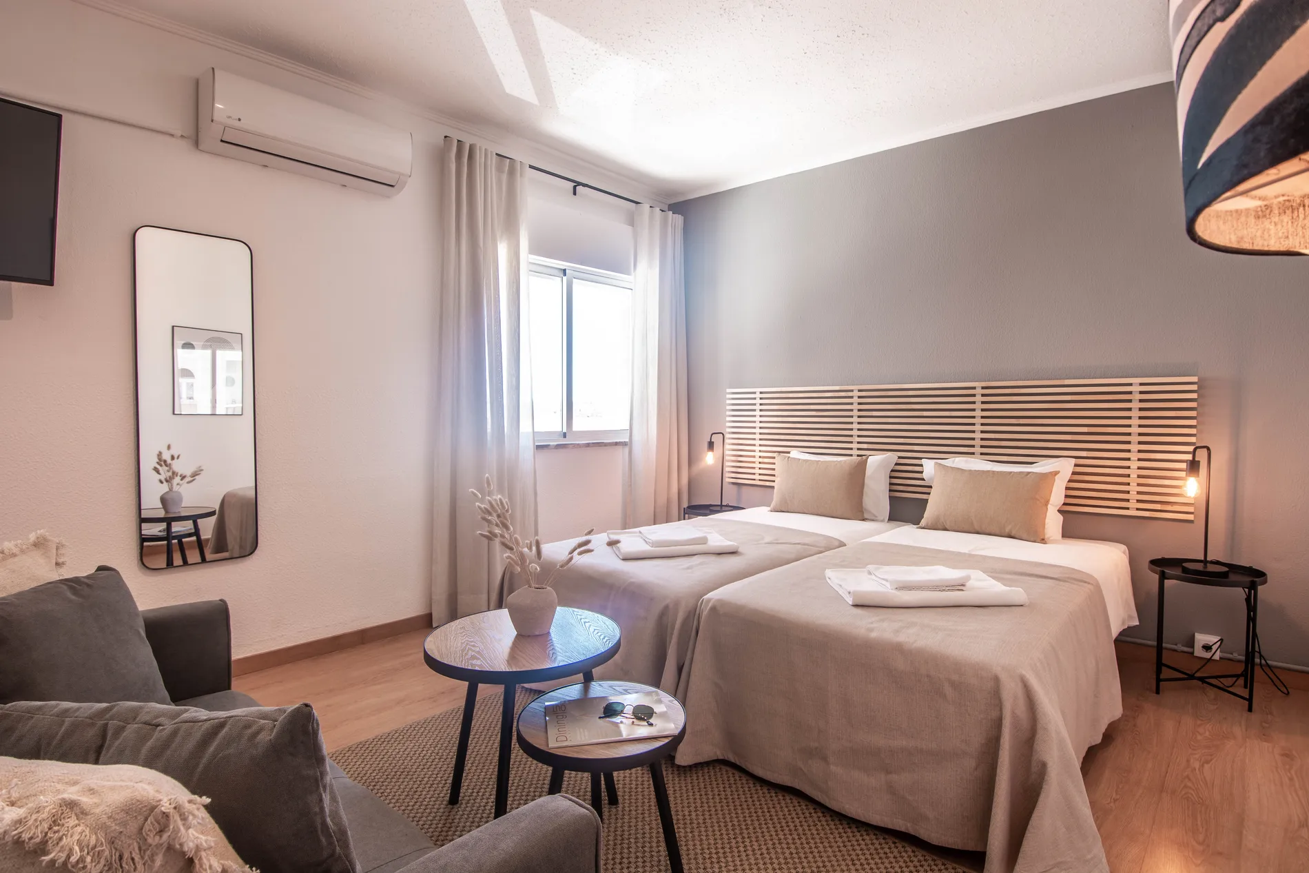 Modern bedroom with twin beds, sofa, and coffee tables near a window.