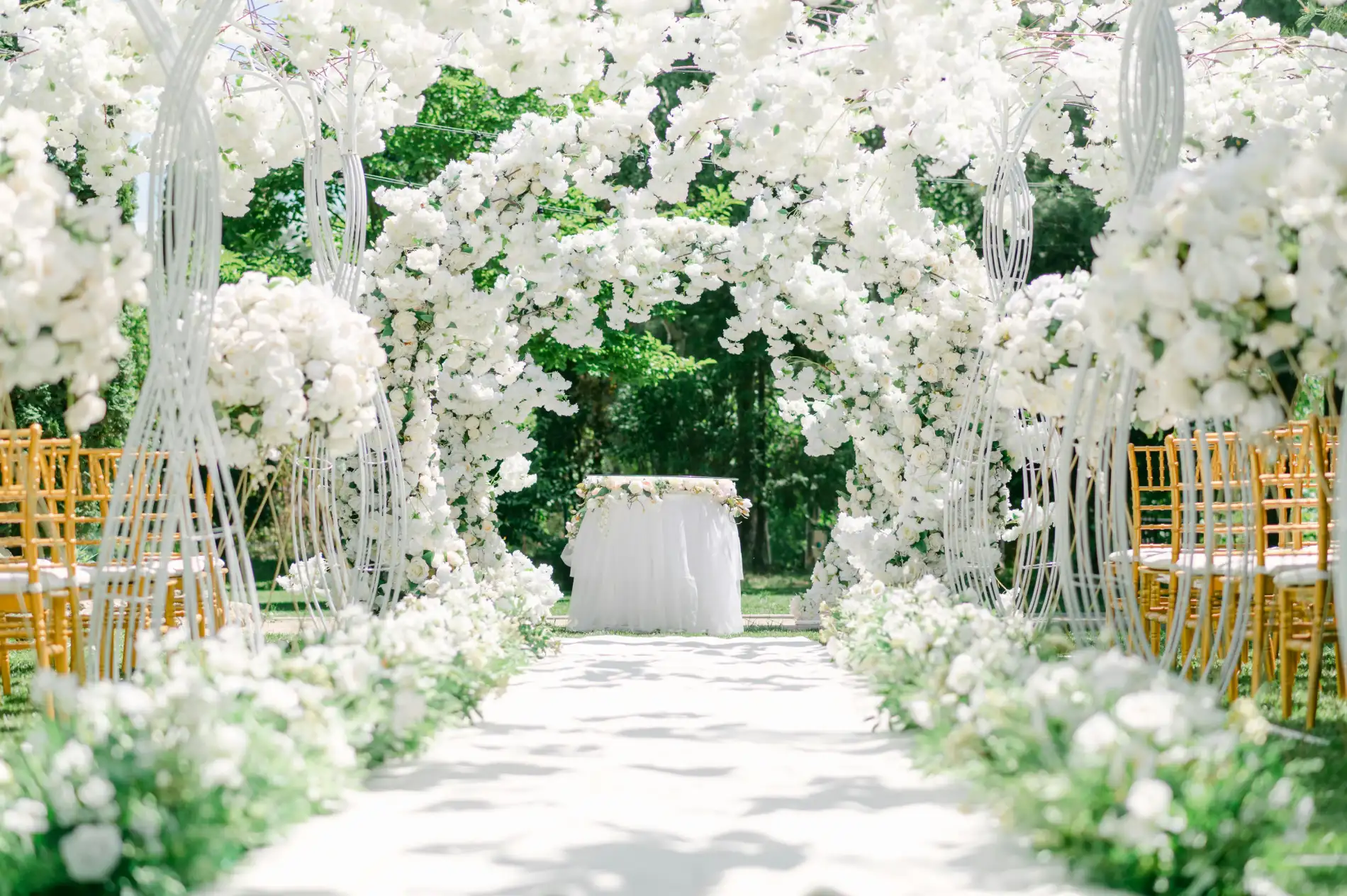 An outdoor wedding aisle with white floral arch and chairs.