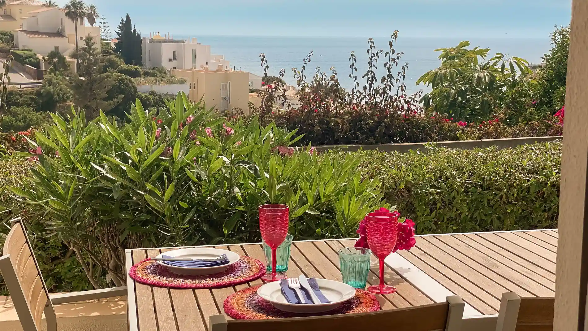 Outdoor table set for two with ocean and greenery in the background.