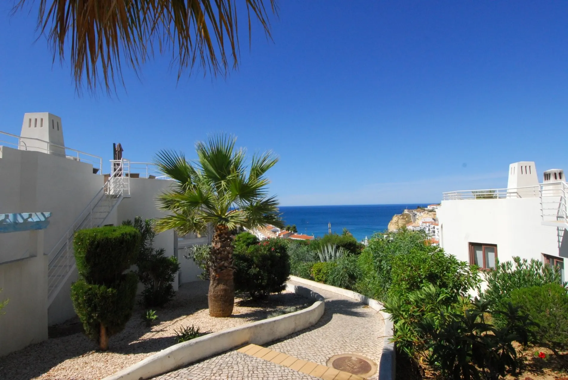 Pathway by a house with a sea view under a clear blue sky.