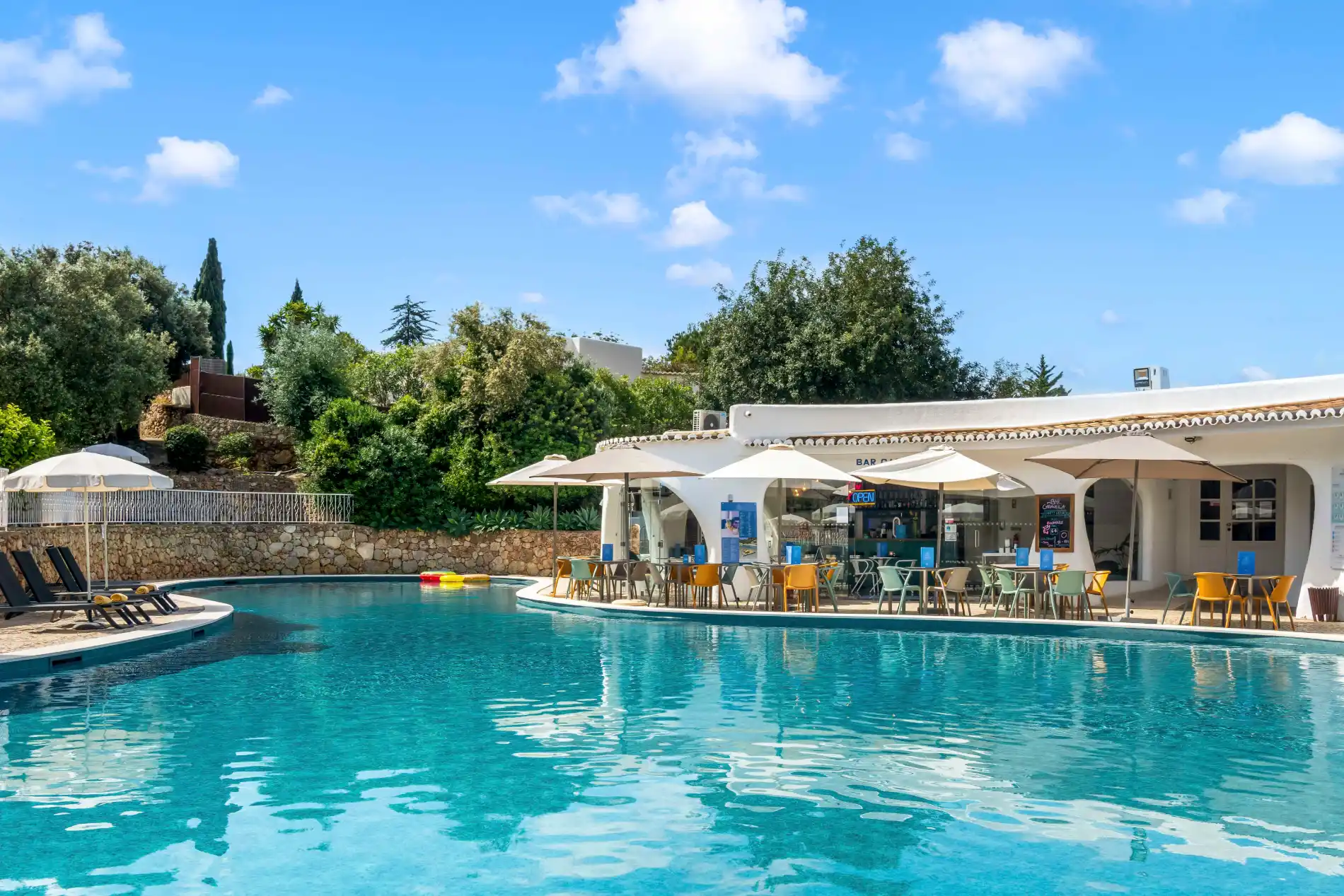 Outdoor pool with a poolside bar and chairs under umbrellas.