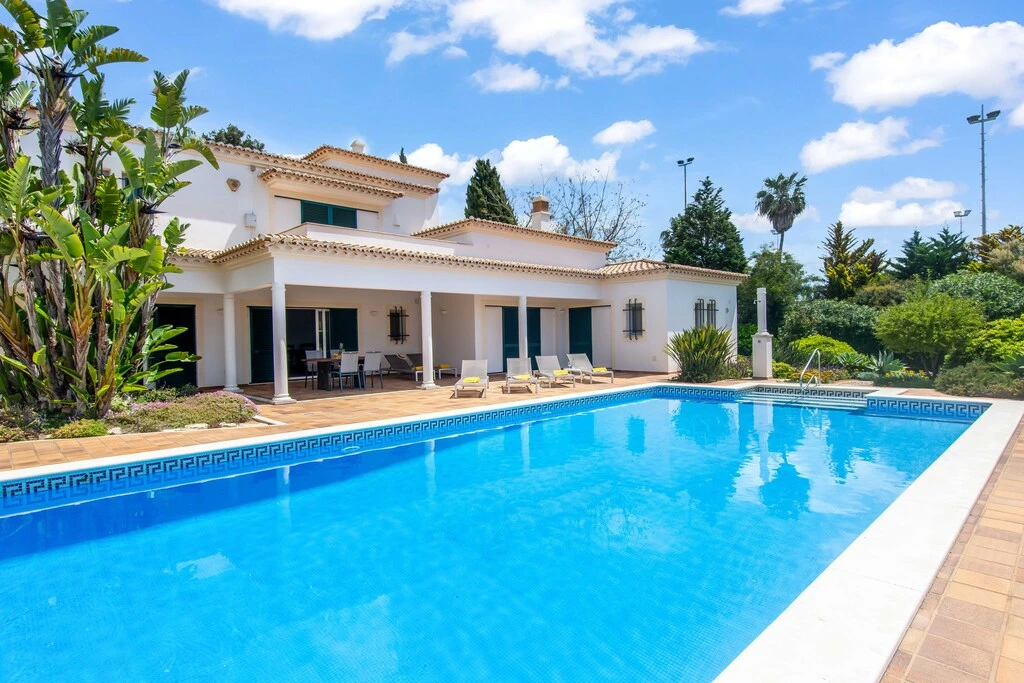 Luxury house with a large pool and patio surrounded by lush greenery.