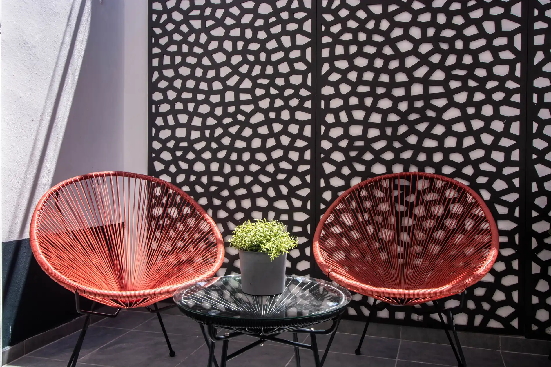 Two red chairs and table with plant in front of patterned screen.
