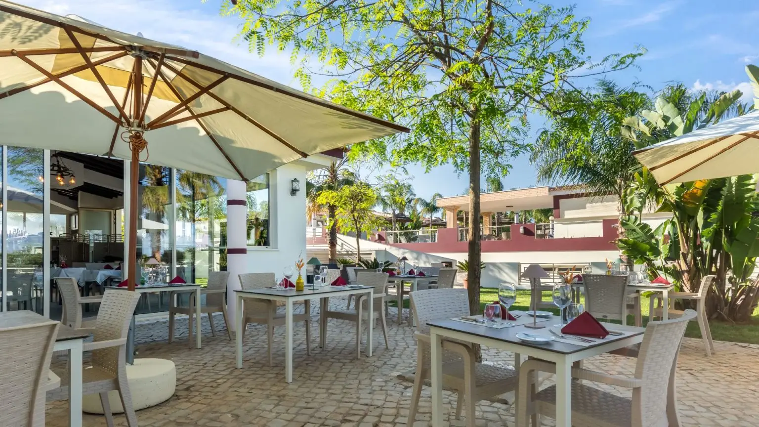 Outdoor dining area with tables under umbrellas, surrounded by greenery.