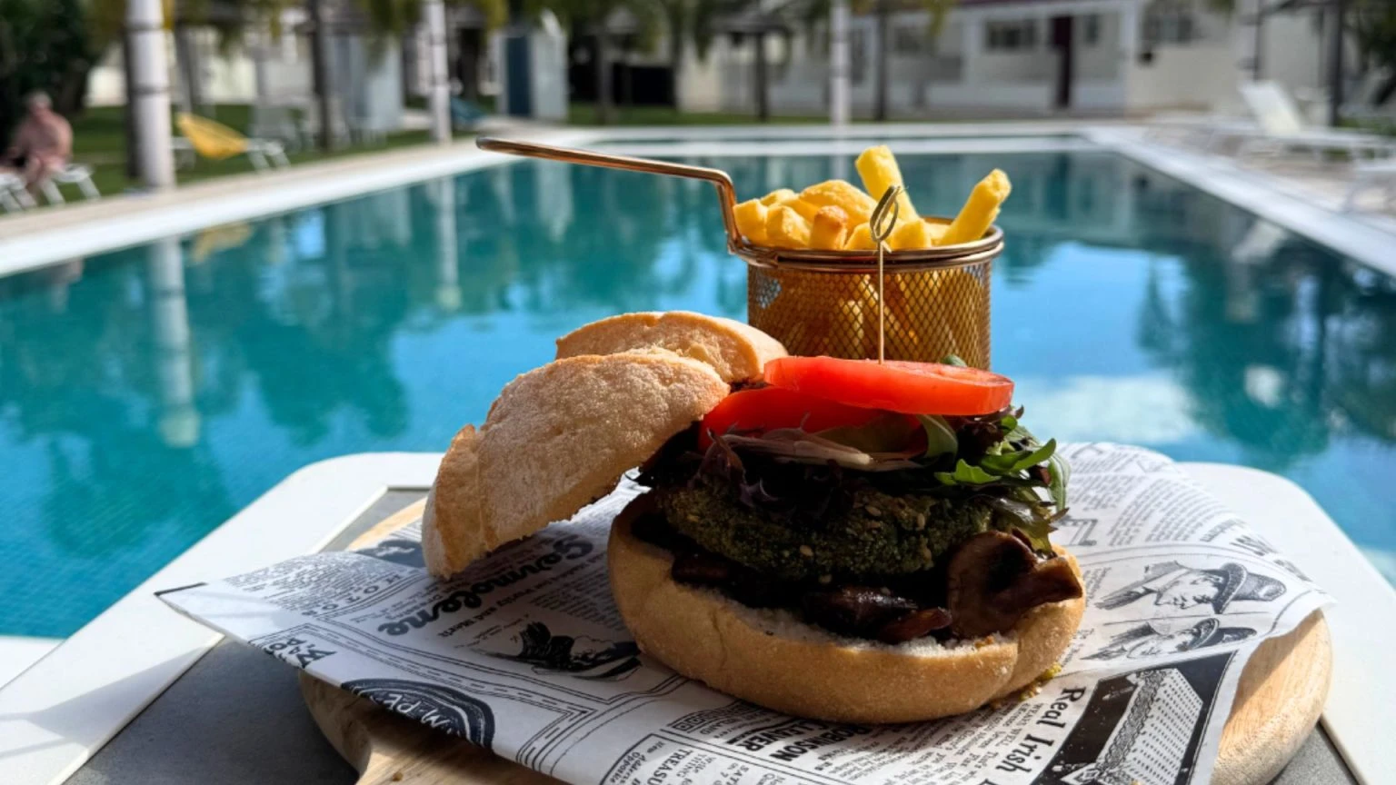 Burger and fries by a poolside table.
