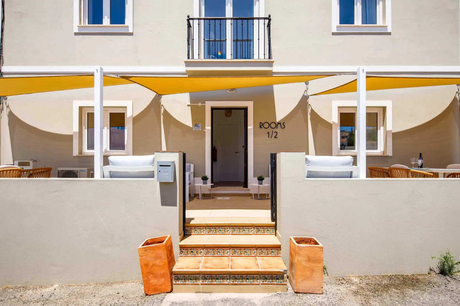 Beige building entrance with yellow awning and terracotta planters.