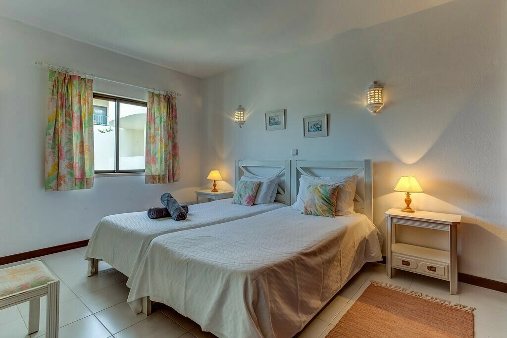 Two twin beds in a cozy, well-lit bedroom with lamps and floral curtains.