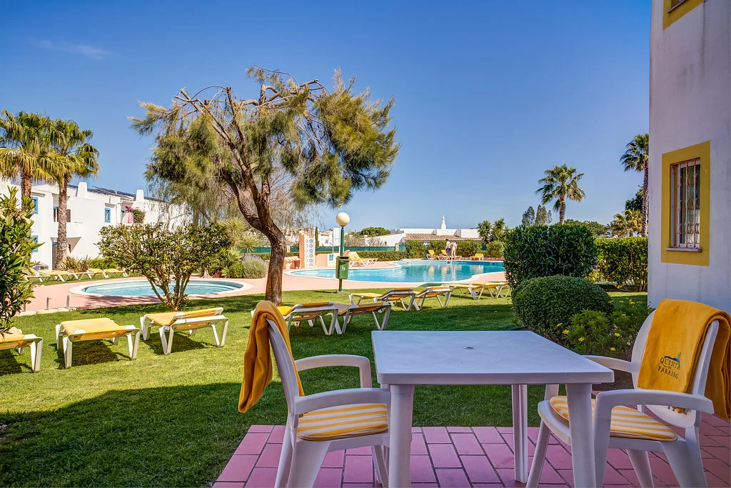 Patio view of a garden with a pool and sun loungers under a clear blue sky.