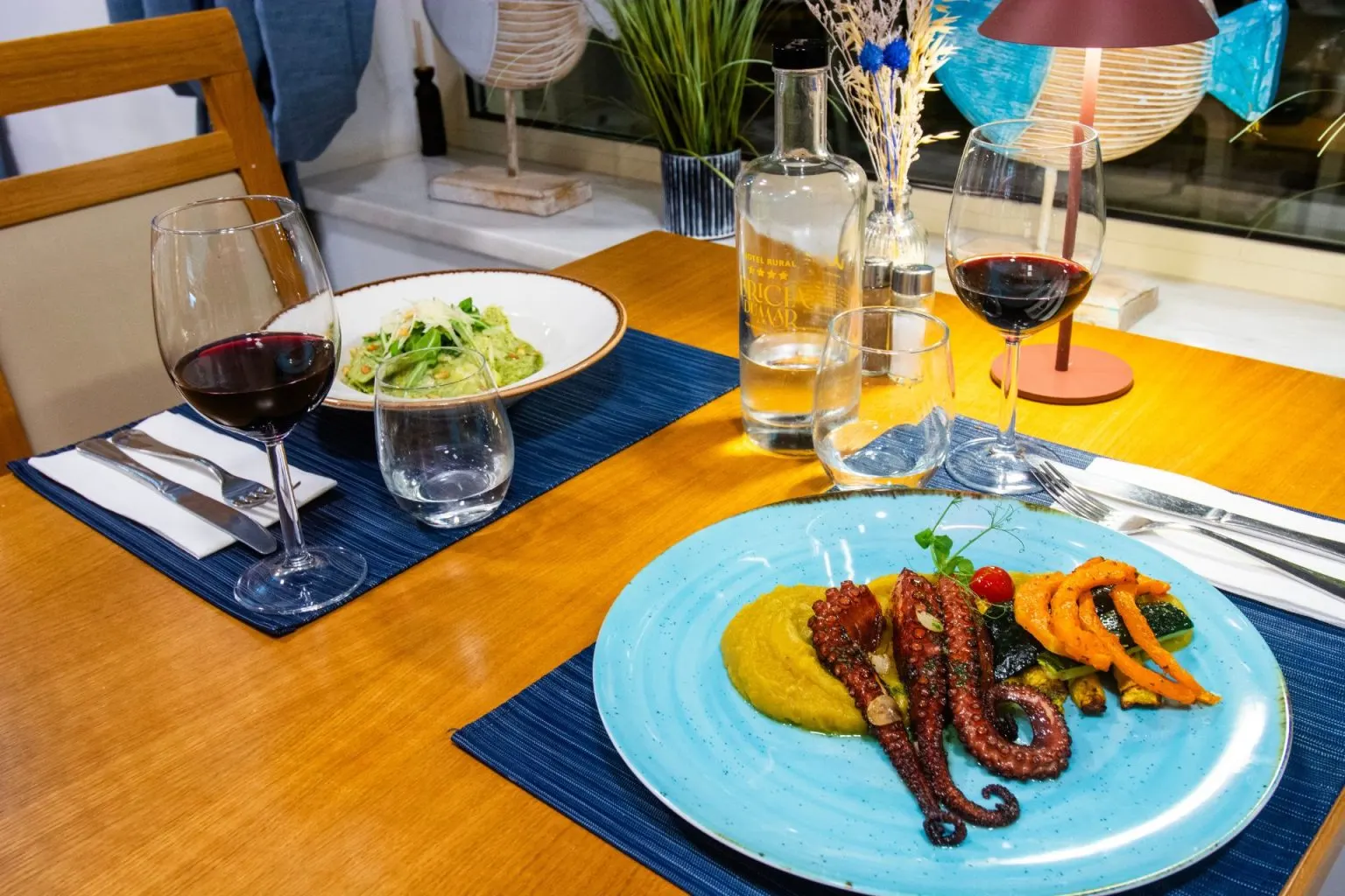 A table set with seafood, pasta, red wine, and water.