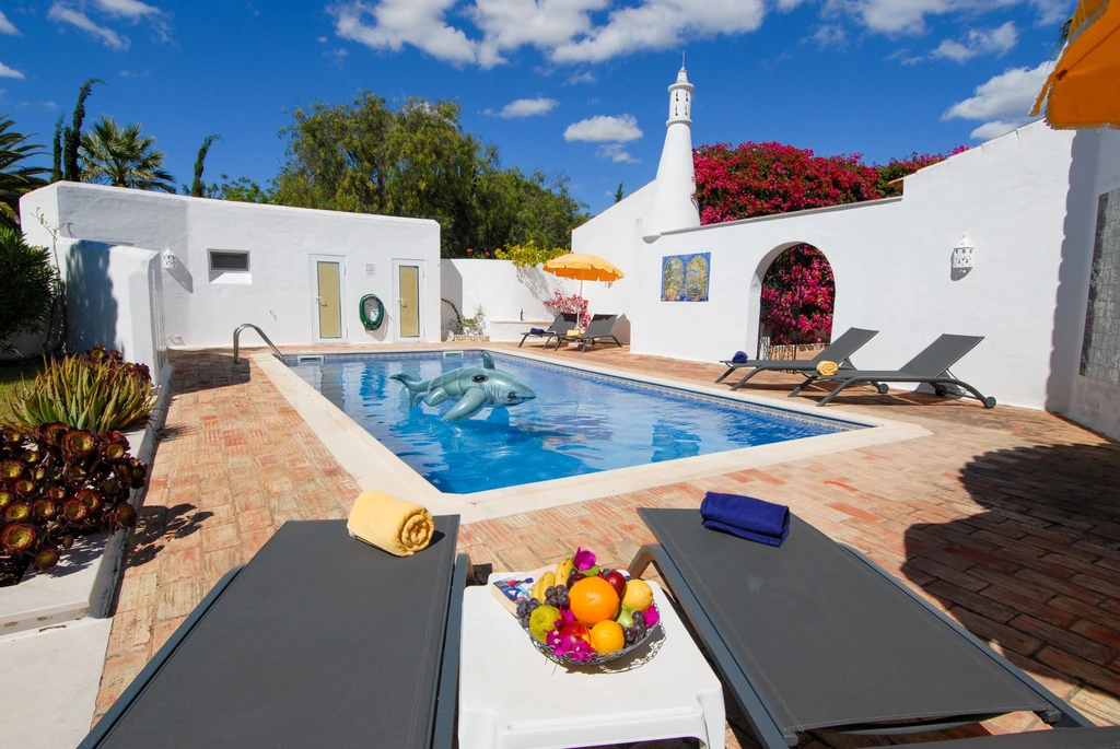 Sunny patio with a pool, sun loungers, and fruit plate.