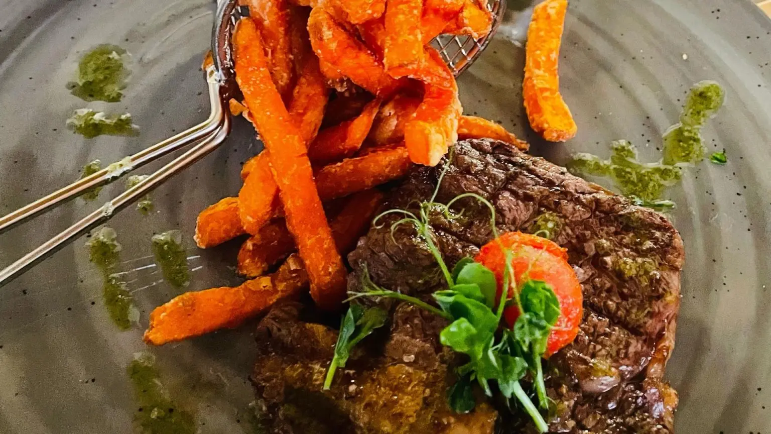 Steak with greens and sweet potato fries on a gray plate.