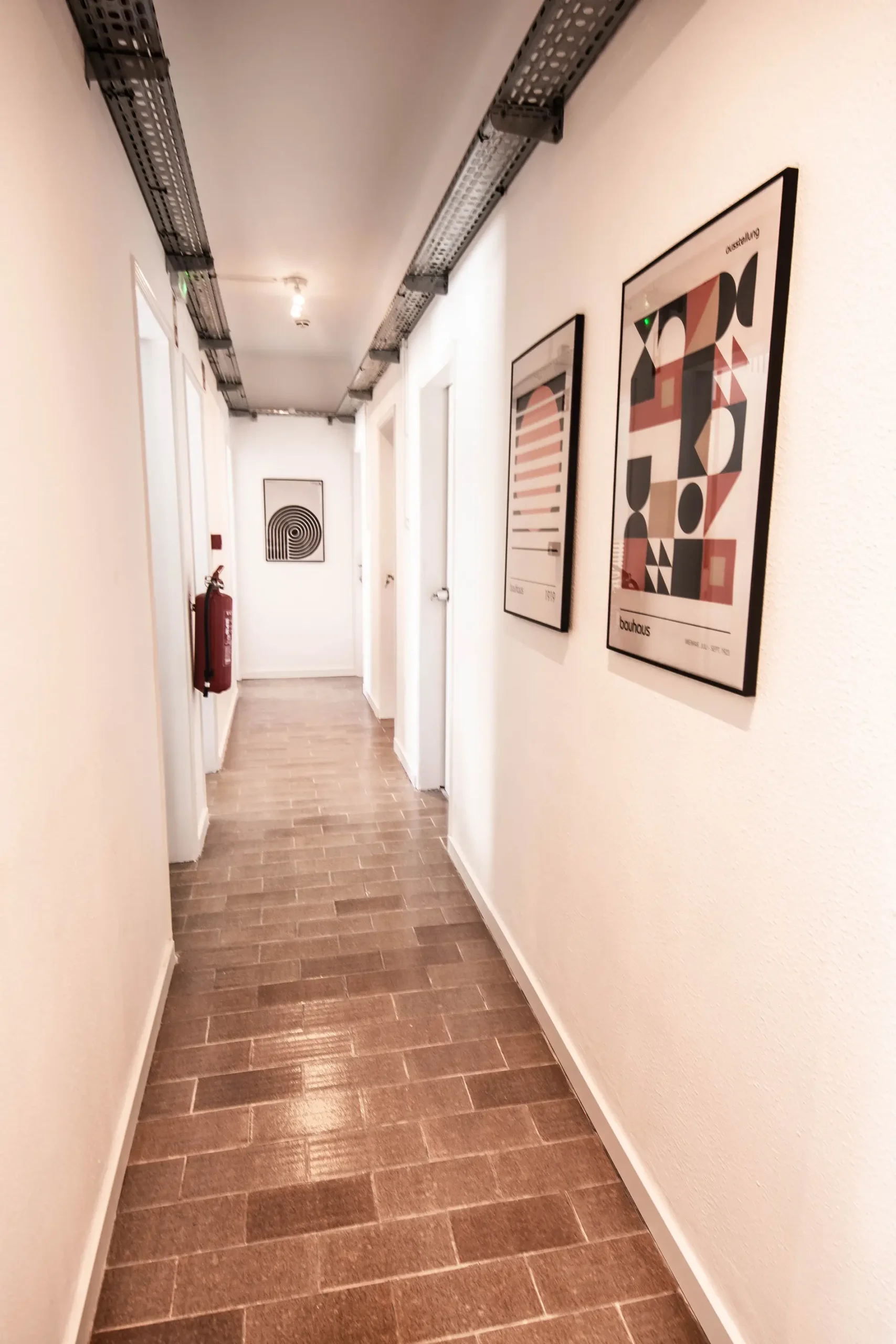 Hallway with framed abstract art and brown brick floor.
