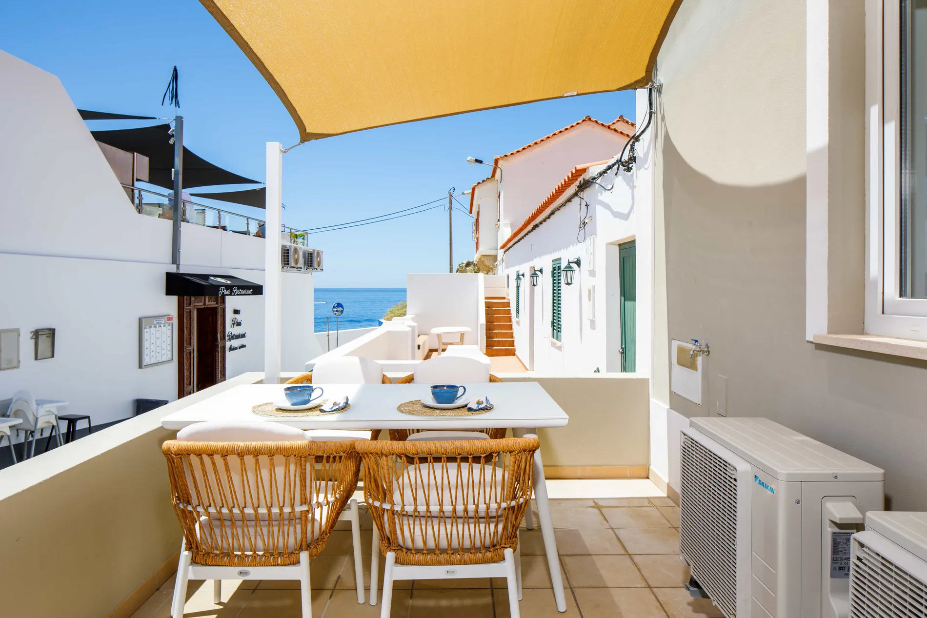 Outdoor dining area with ocean view, shaded by a yellow canopy.