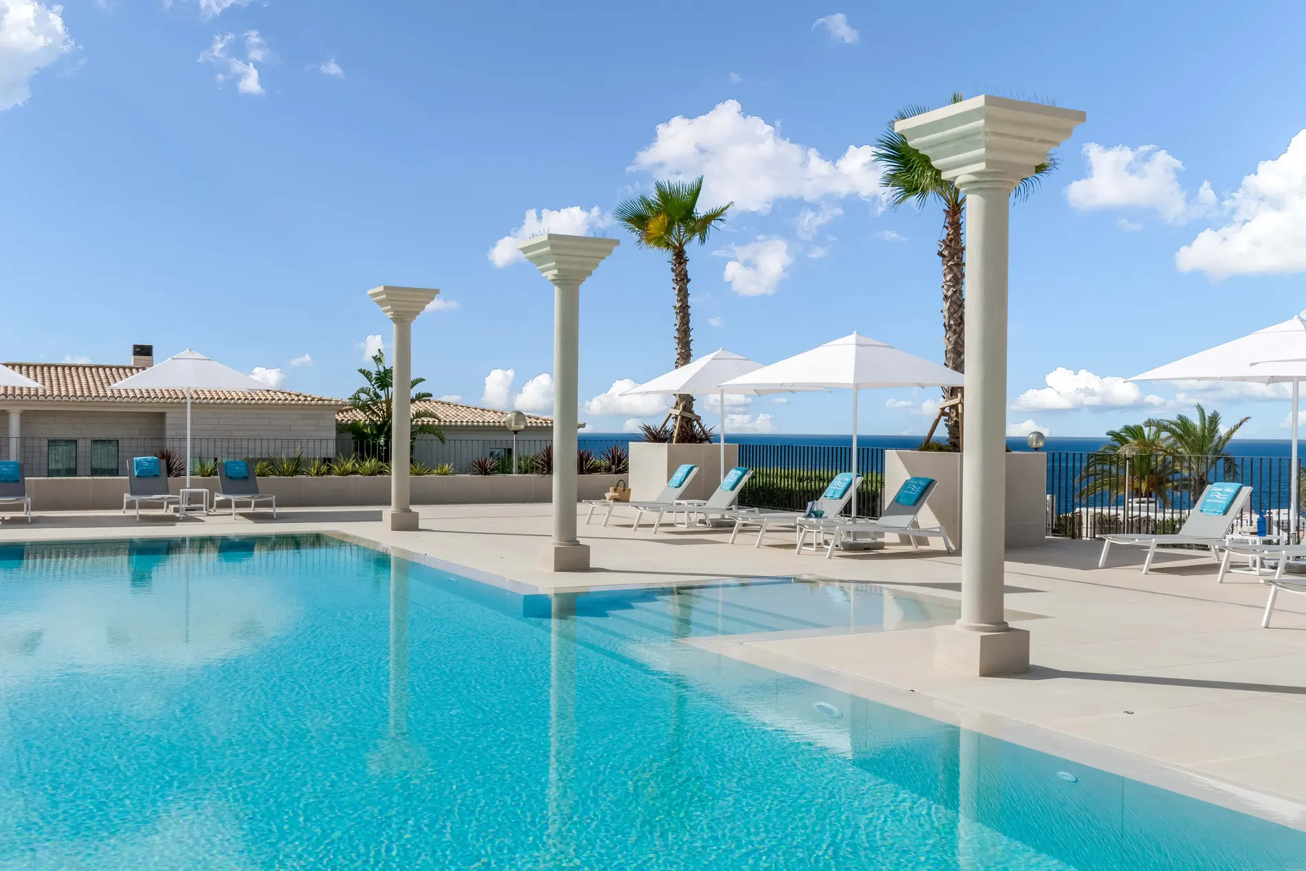 Poolside view with chairs and umbrellas, overlooking the ocean and palm trees.