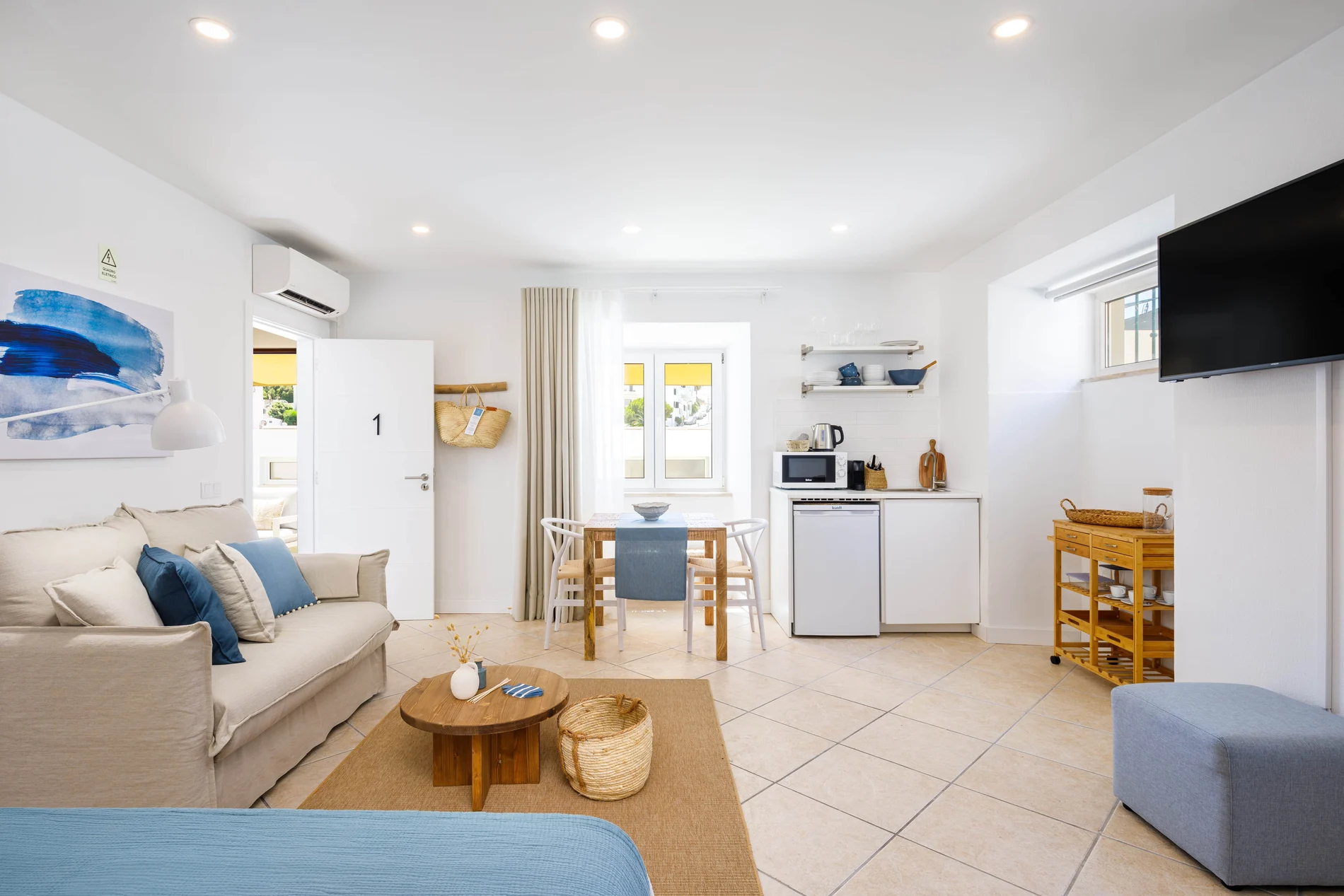 Compact white room with a sofa, dining table, and kitchenette.