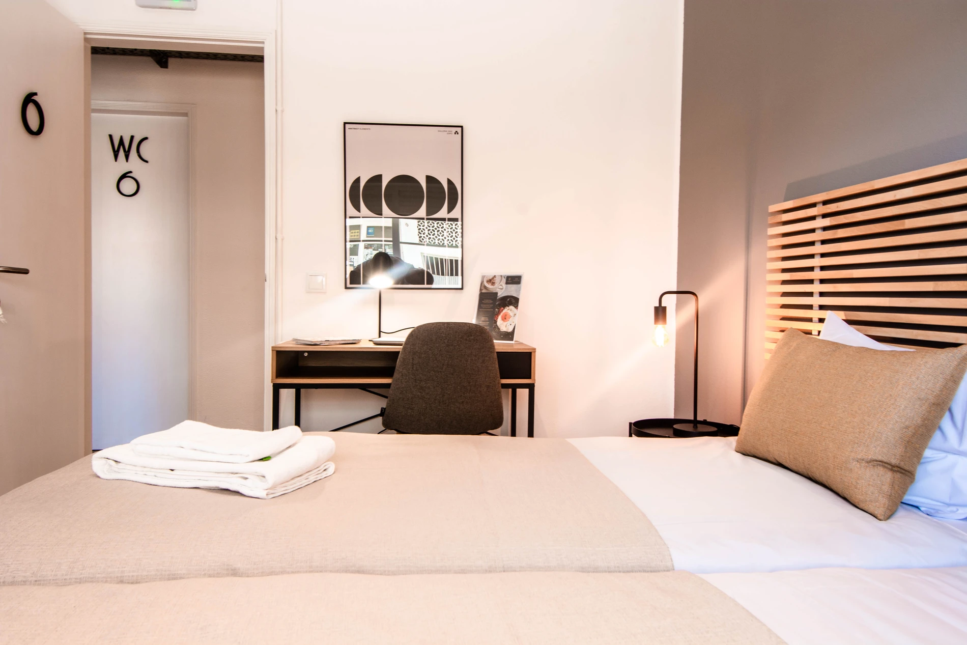 Modern bedroom with a bed, desk, chair, and a lamp by the bedside.