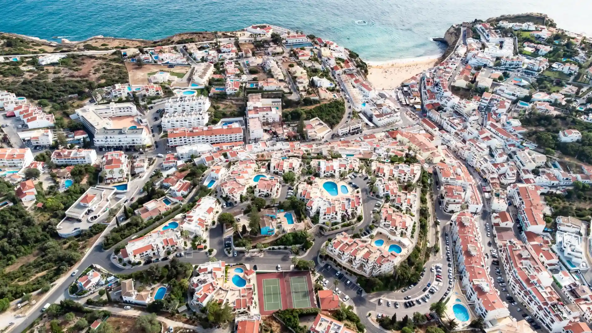 Aerial view of a coastal town with pools, roads, and the sea.