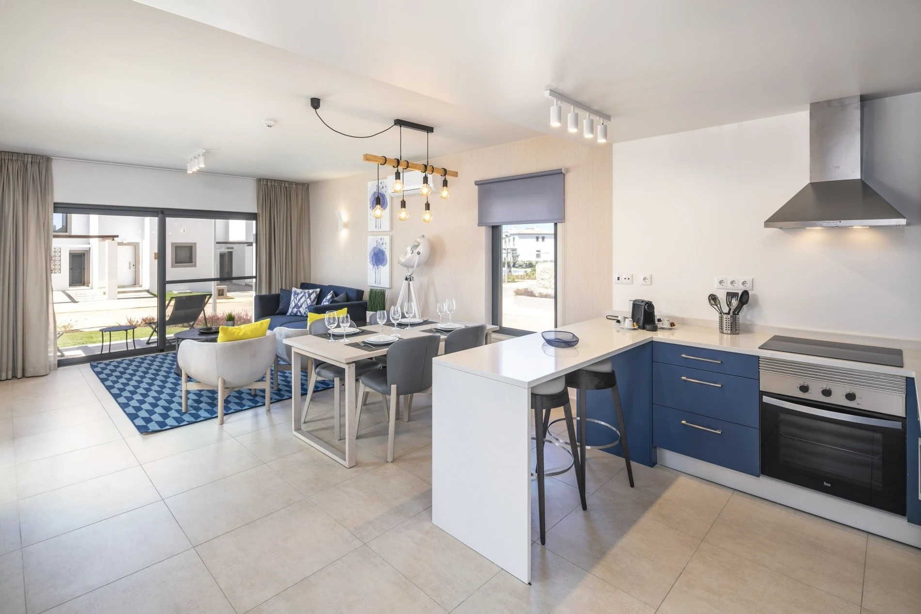 Modern open-plan living room and kitchen with blue accents and large windows.