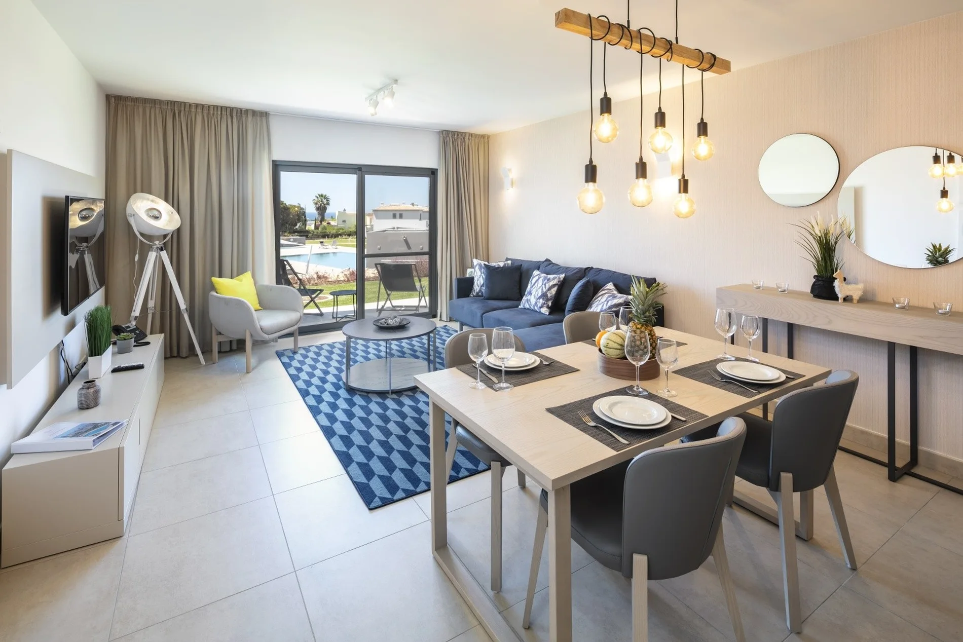 Modern living room with dining table, sofa, large window, and stylish lighting.