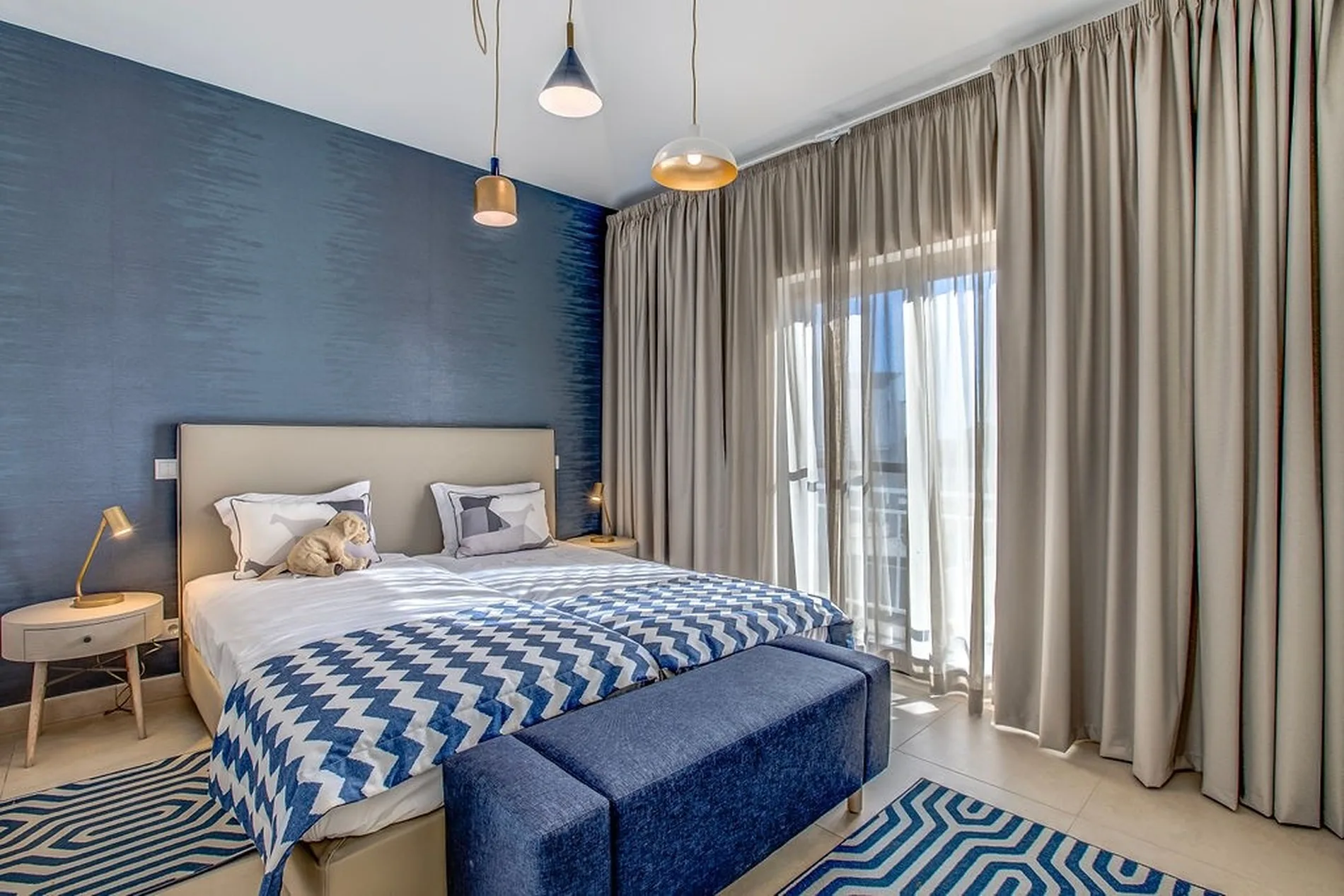 Bedroom with blue accents, patterned blanket, curtains, and pendant lights.