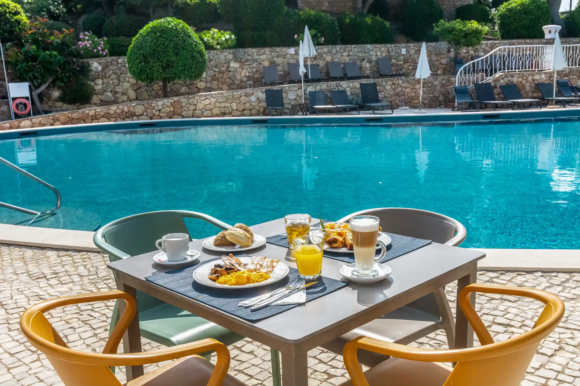 Breakfast by the pool with orange juice and coffee in a sunny setting.
