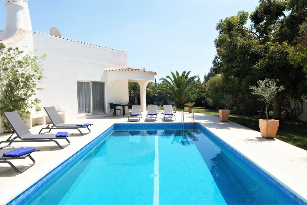 White villa with pool, sun loungers, and garden with trees.
