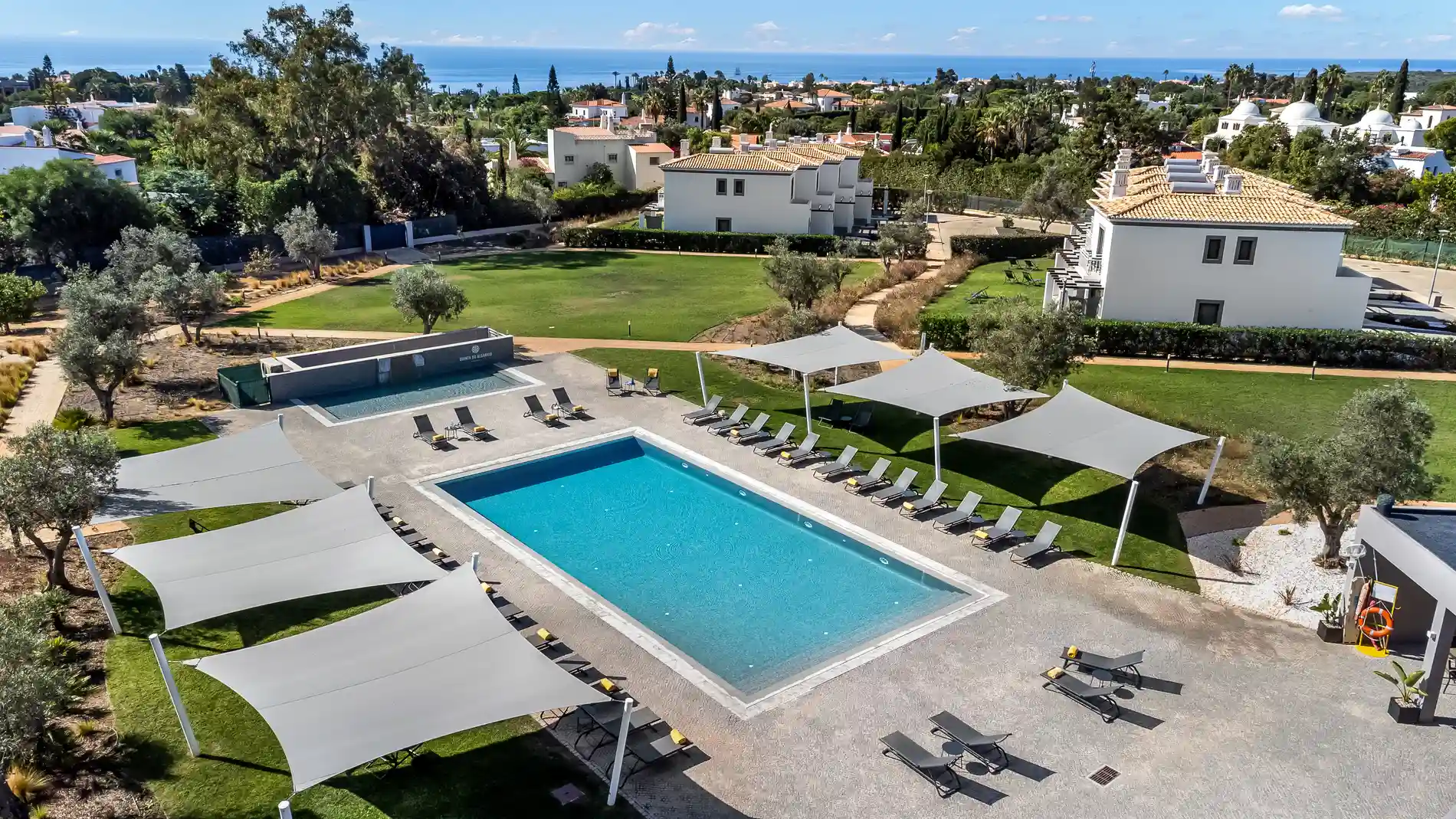 Aerial view of a pool with sun loungers and shade structures in a grassy area.