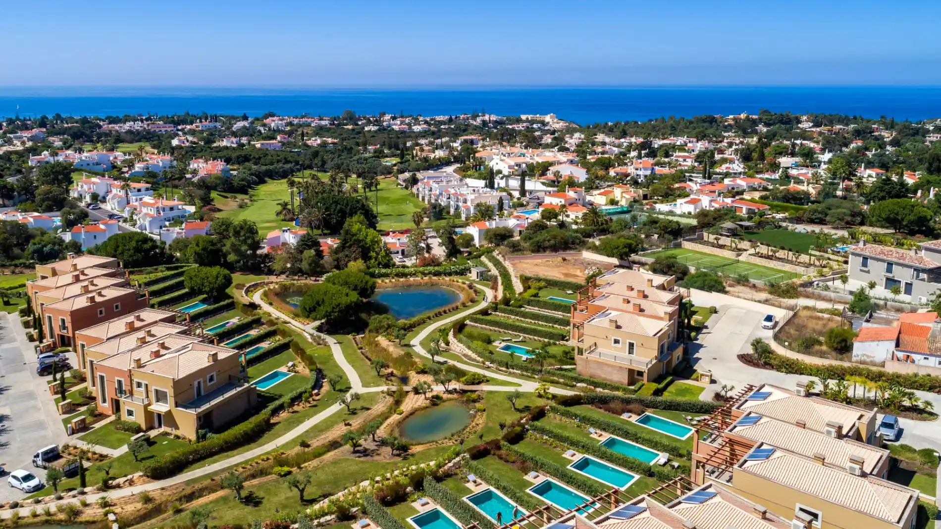 Aerial view of a coastal village with villas and pools by the sea.