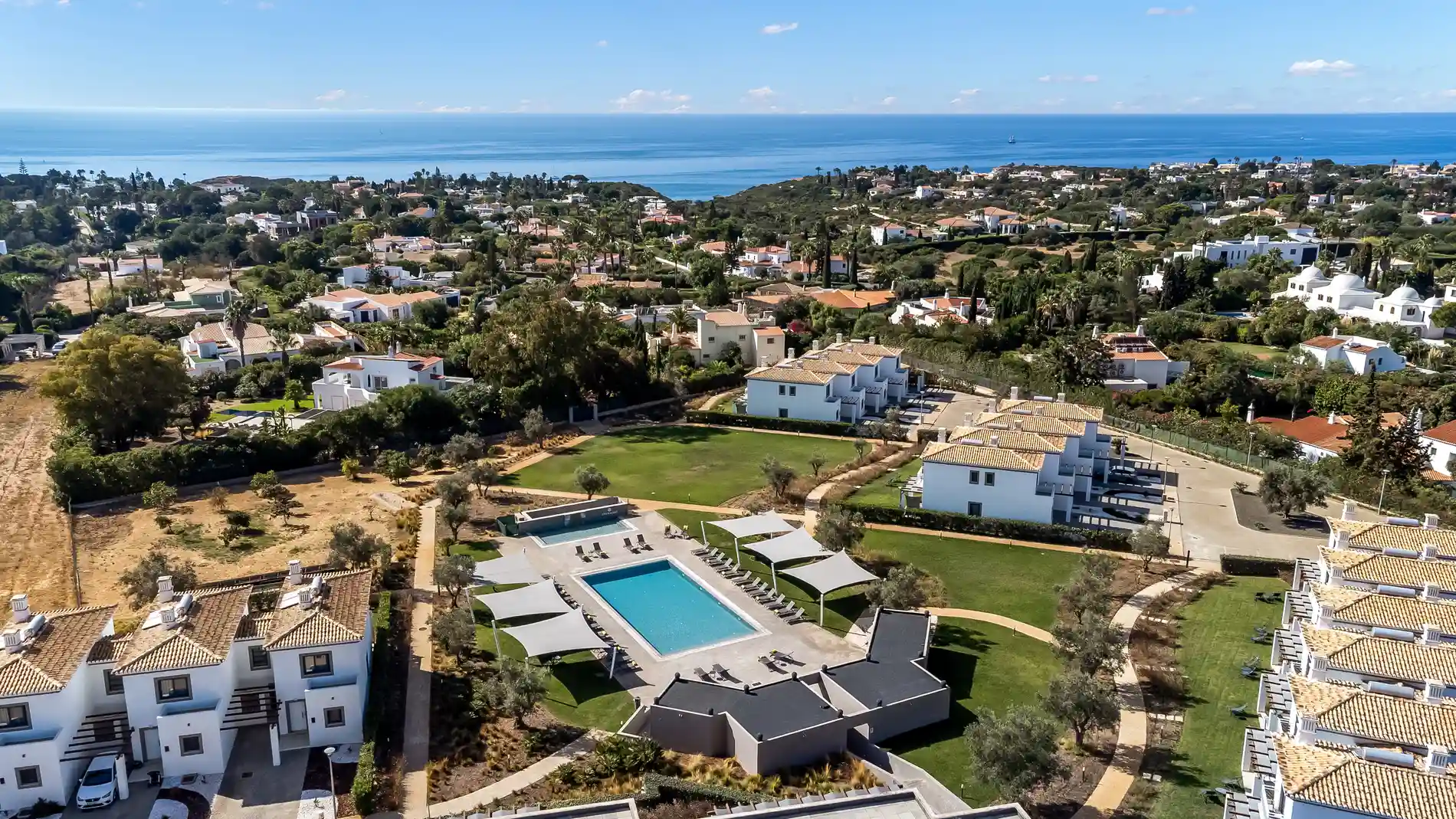 Aerial view of houses, a pool, and greenery by the sea.