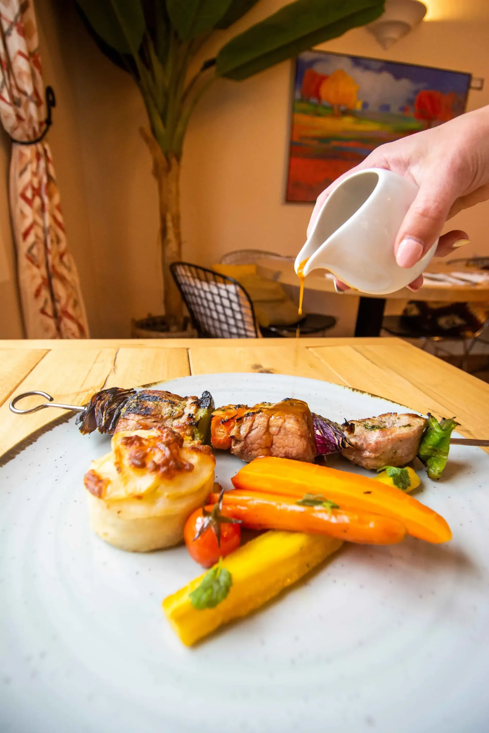 Plated dish with meat skewer, carrots, and sauce being poured.