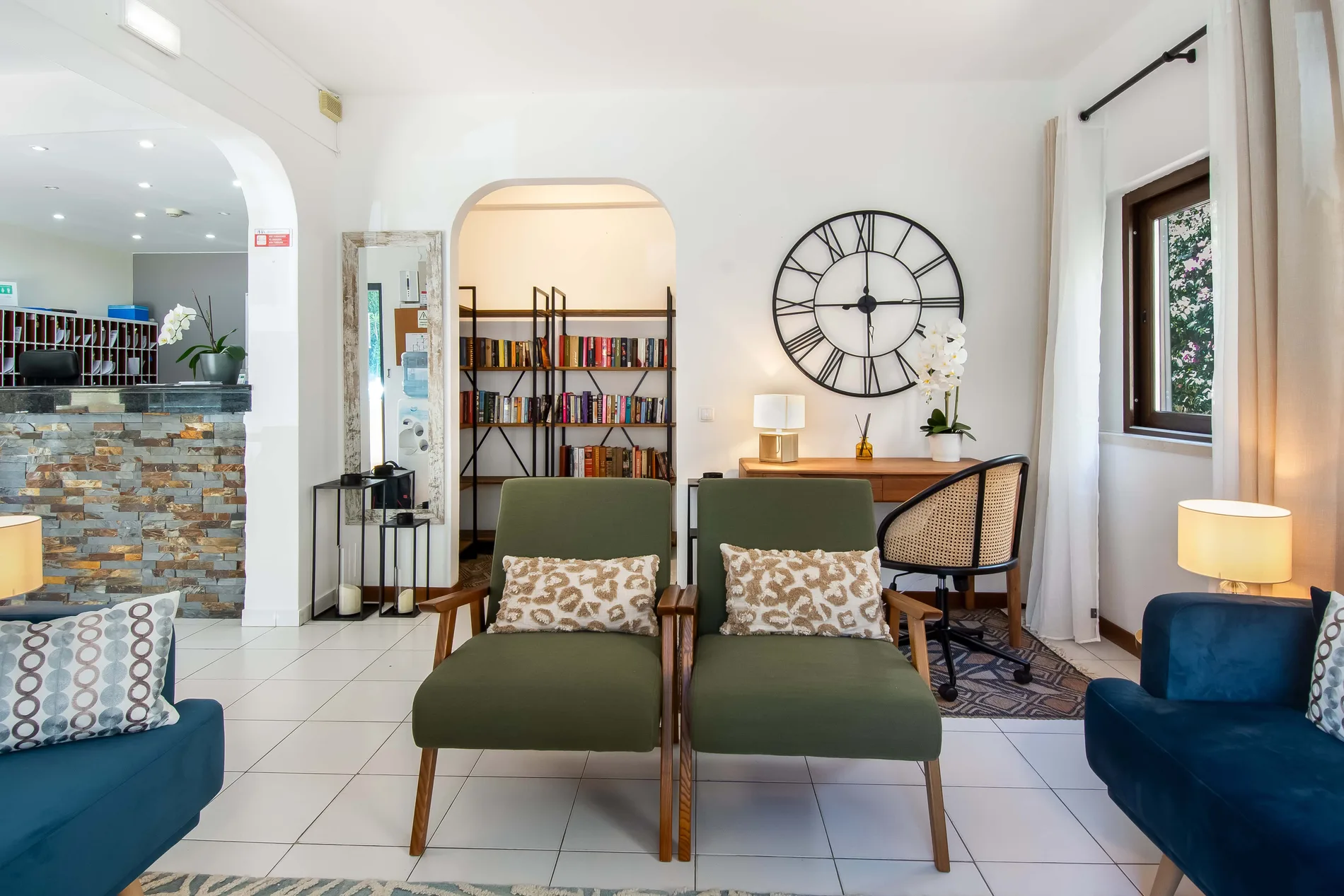 Cozy living room with green chairs, bookshelf, and large clock on the wall.