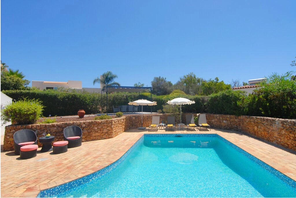 Outdoor pool with loungers and umbrellas, surrounded by trees and stone walls.