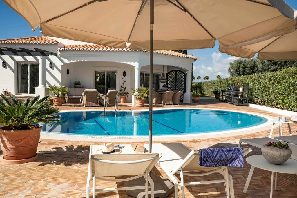 Sunlit poolside patio with lounge chairs and parasols.