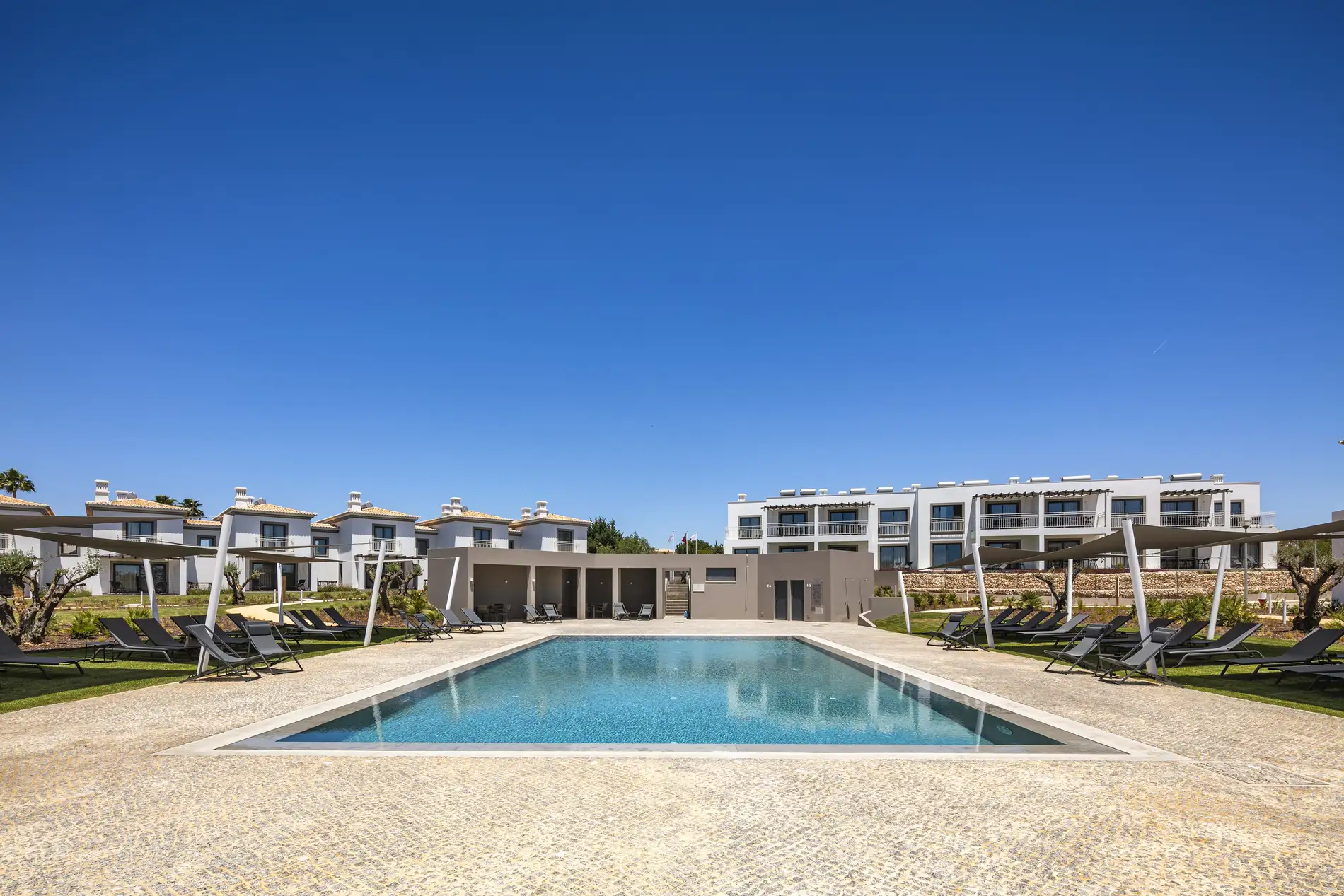 Modern villas with a pool and sun loungers under a clear blue sky.