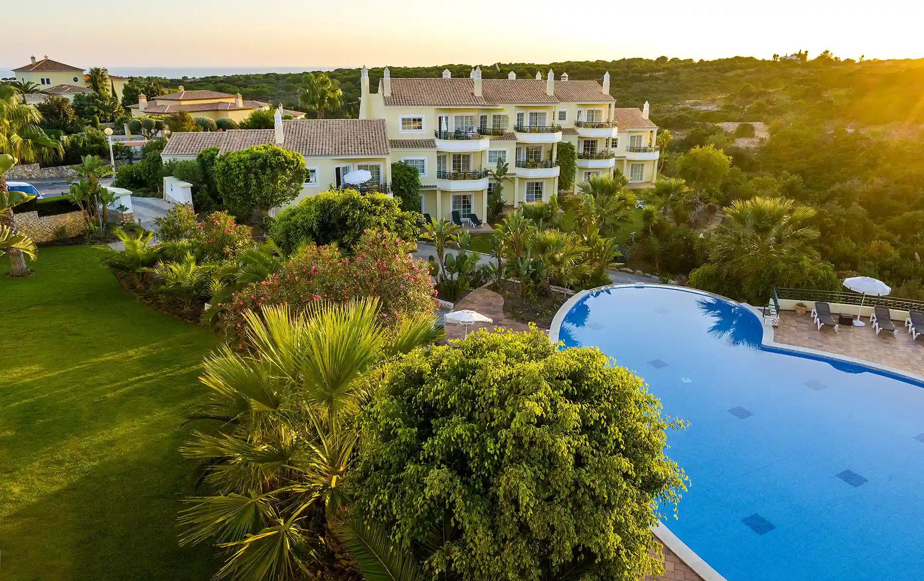 Large villa with pool and lush garden at sunset.