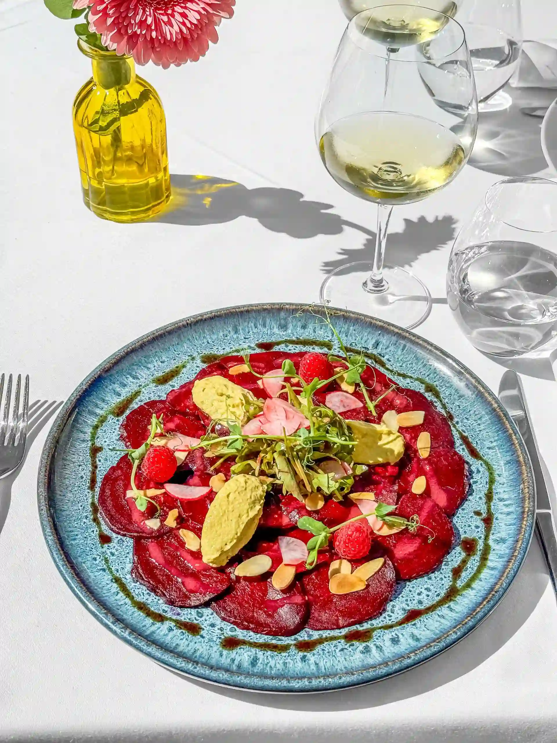 Colorful beet carpaccio with a glass of white wine on a table.