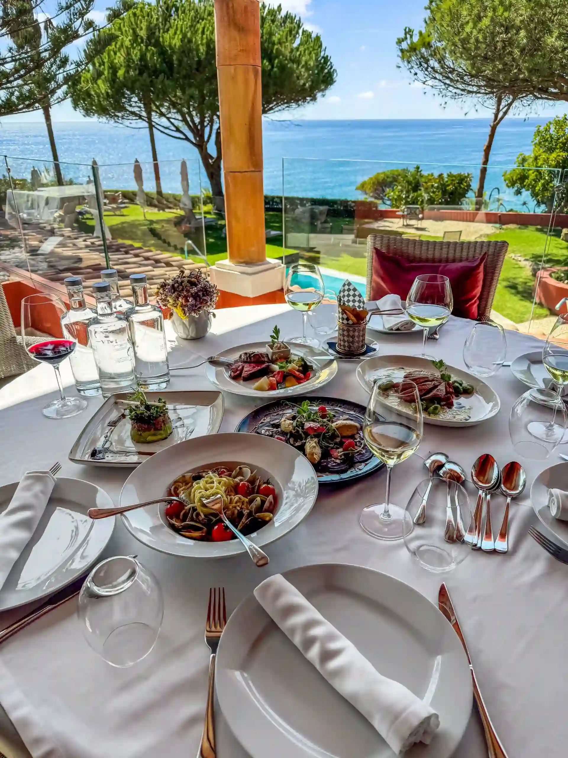 Outdoor dining with pasta, wine, and ocean view.
