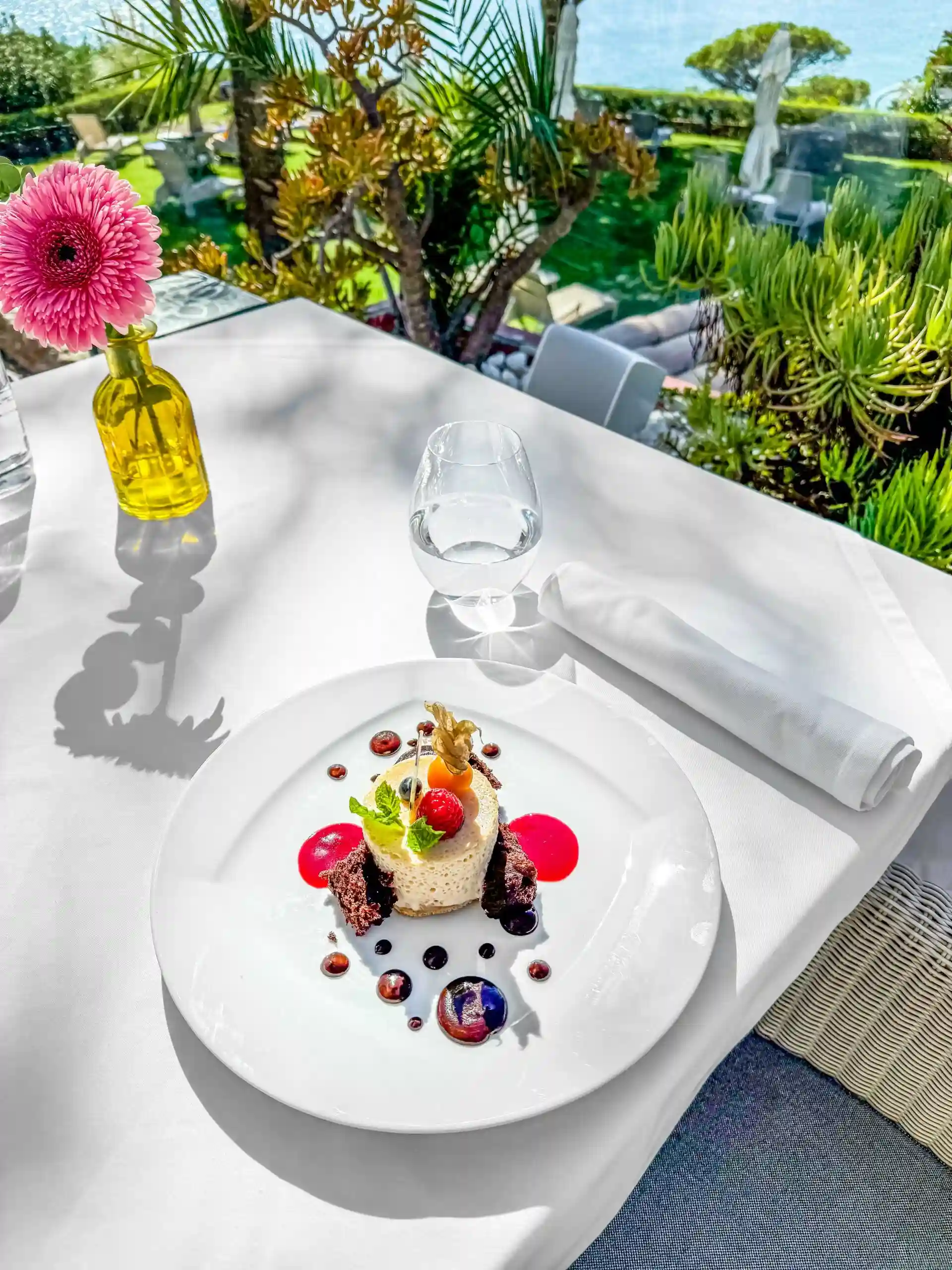 Dessert on a table by a window, with a pink flower and sunny garden view.