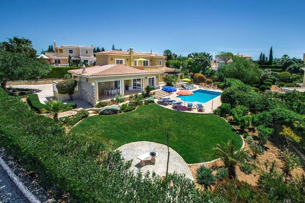 Aerial view of a villa with a pool, garden, and patio under a clear blue sky.