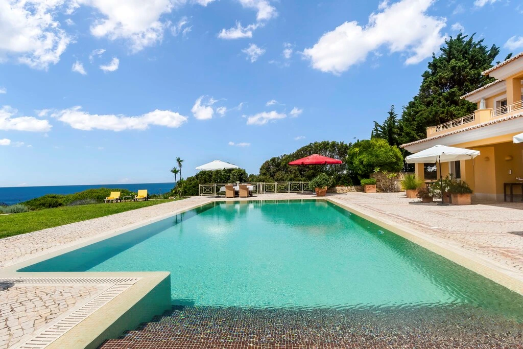 Outdoor pool with umbrellas and ocean view under a blue sky.