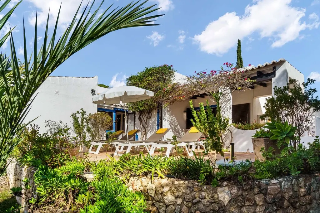 White villa with sun loungers and garden, set against a bright blue sky.