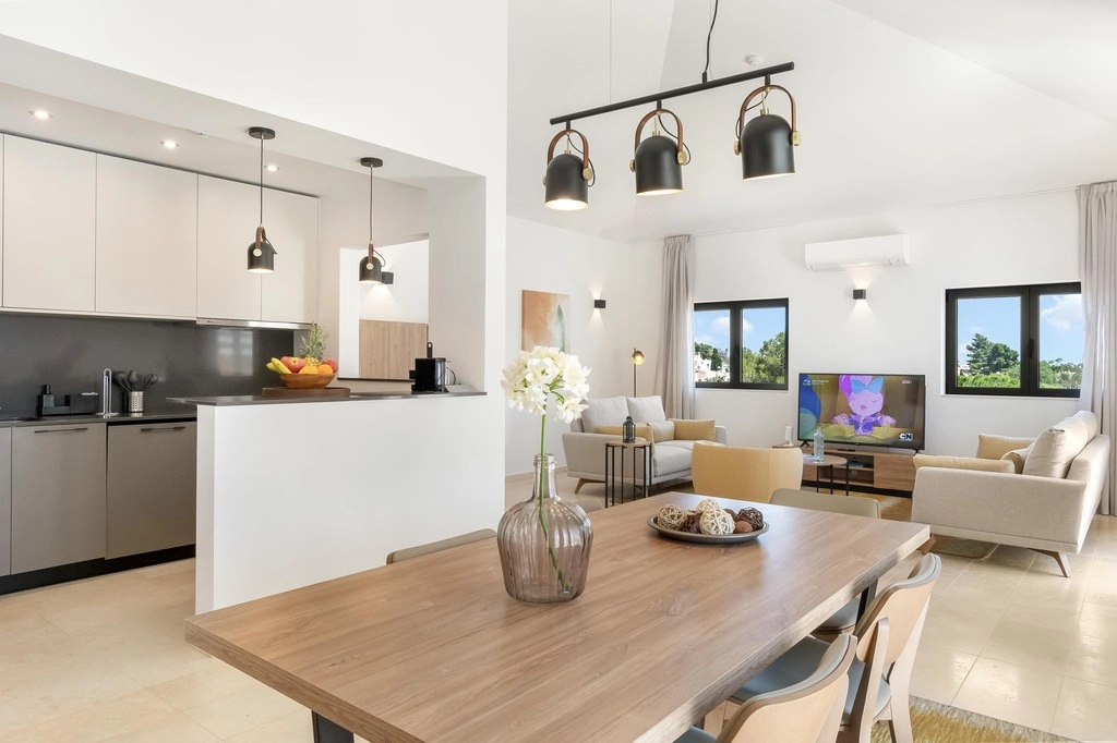 Modern open living room with kitchen, wooden table, and pendant lights.
