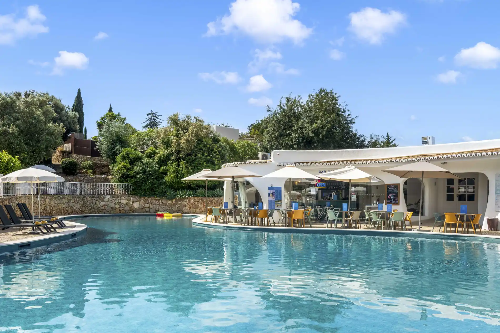Poolside cafe with umbrellas and chairs by a clear blue swimming pool.