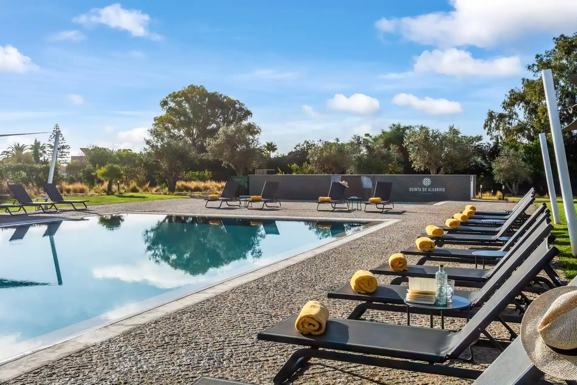 Poolside loungers with yellow towels under a clear blue sky.