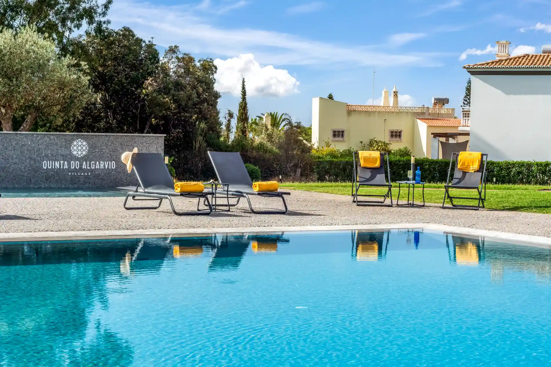 Poolside with lounge chairs and towels under a sunny sky.