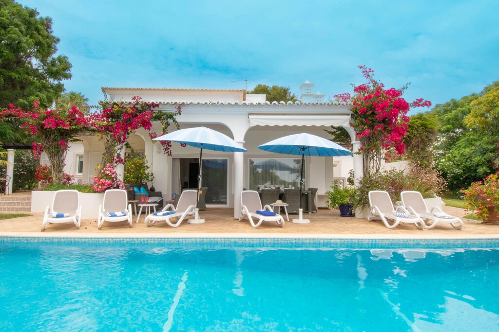 Poolside view of a villa with lounge chairs and umbrellas.