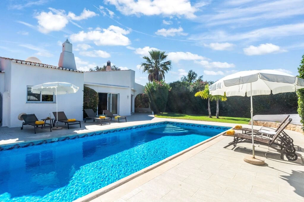 Outdoor pool and lounge chairs in a sunny backyard setting.